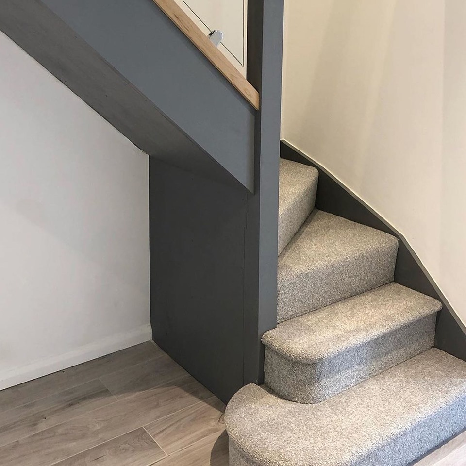 Close up shot of the foot of a winder staircase painted and carpeted in grey